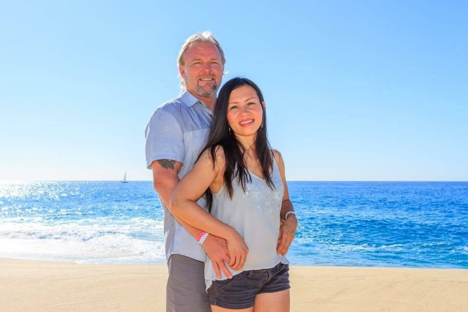 Michael Agee and his wife Thao smiling together at the beach.